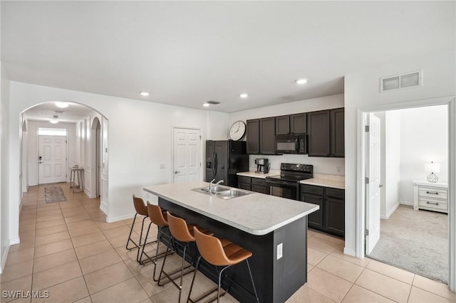 kitchen featuring visible vents, arched walkways, an island with sink, black appliances, and a sink