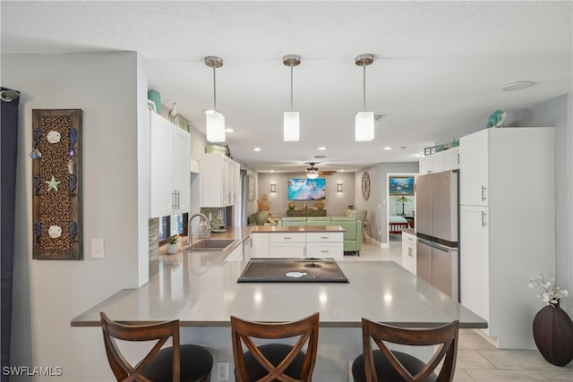 kitchen featuring kitchen peninsula, sink, stainless steel fridge, a kitchen bar, and white cabinets