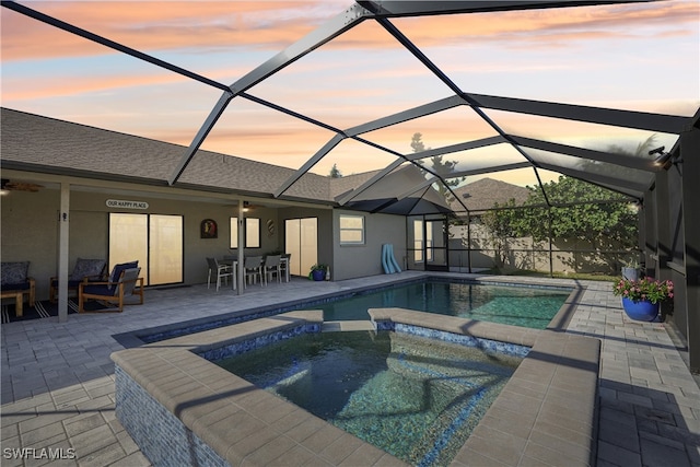 pool at dusk with a patio area, an in ground hot tub, and glass enclosure