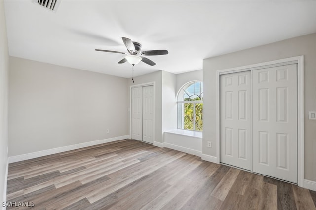 unfurnished bedroom with light wood-type flooring, ceiling fan, and multiple closets