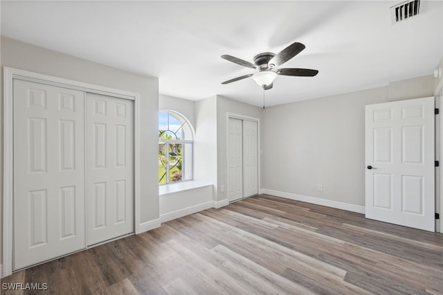 unfurnished bedroom with ceiling fan, light hardwood / wood-style flooring, and two closets