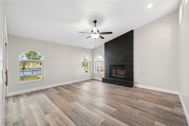 unfurnished living room featuring ceiling fan, a fireplace, vaulted ceiling, and light wood-type flooring