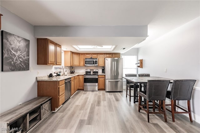 kitchen with sink, stainless steel appliances, light hardwood / wood-style floors, and a skylight