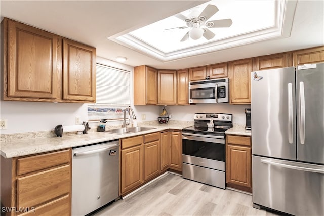 kitchen featuring light hardwood / wood-style flooring, stainless steel appliances, a tray ceiling, sink, and ceiling fan