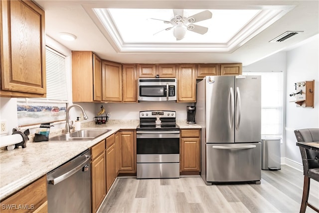 kitchen with stainless steel appliances, a tray ceiling, sink, light wood-type flooring, and ceiling fan