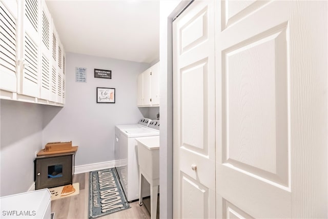 clothes washing area featuring separate washer and dryer, light wood-type flooring, and cabinets