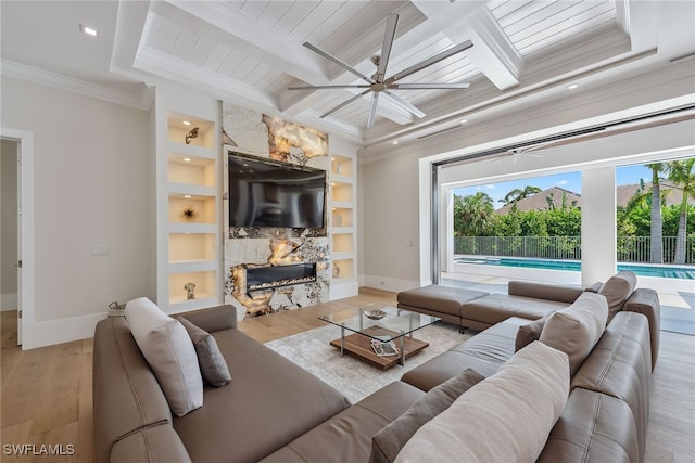 living room featuring ornamental molding, beamed ceiling, a fireplace, built in shelves, and light hardwood / wood-style floors