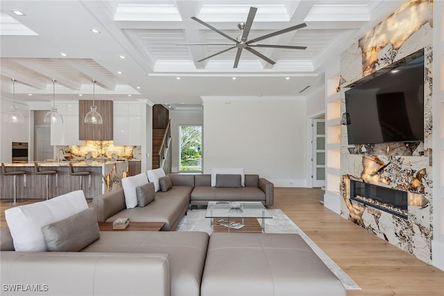 living room with a stone fireplace, ceiling fan, beam ceiling, ornamental molding, and light hardwood / wood-style flooring