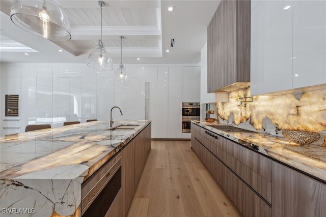 kitchen featuring beamed ceiling, hanging light fixtures, sink, light wood-type flooring, and white cabinetry