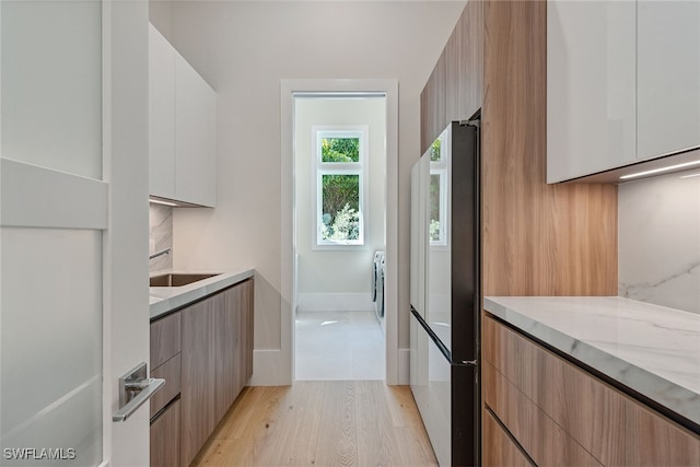 kitchen with sink, light stone countertops, stainless steel fridge, light wood-type flooring, and white cabinetry