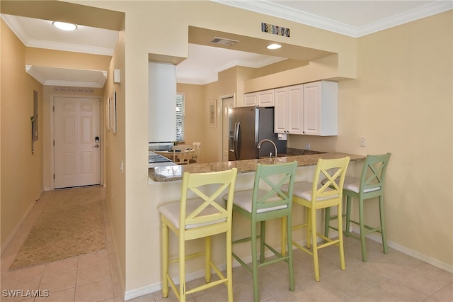 kitchen with a kitchen bar, kitchen peninsula, white cabinets, crown molding, and stainless steel fridge with ice dispenser