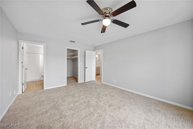 unfurnished bedroom with ensuite bathroom, a spacious closet, a closet, ceiling fan, and light colored carpet