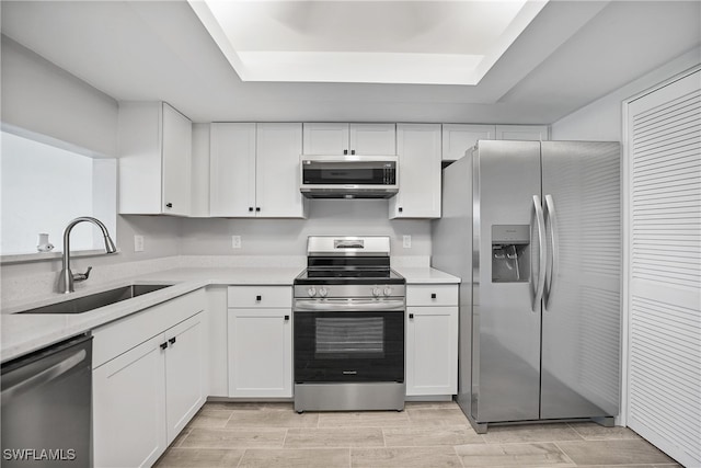 kitchen with sink, appliances with stainless steel finishes, white cabinets, and a raised ceiling