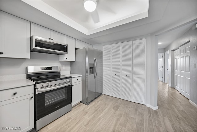 kitchen featuring appliances with stainless steel finishes, light hardwood / wood-style flooring, white cabinets, and a raised ceiling