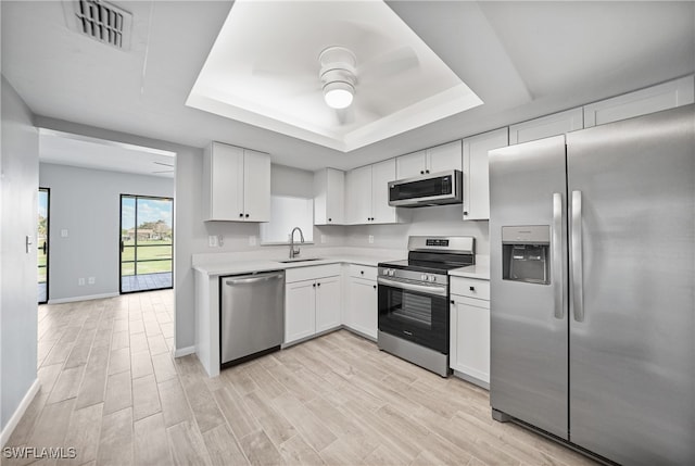 kitchen featuring sink, a raised ceiling, light hardwood / wood-style floors, stainless steel appliances, and white cabinets