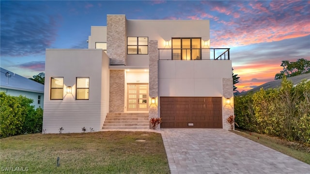 contemporary home with a balcony, decorative driveway, french doors, a front lawn, and stucco siding