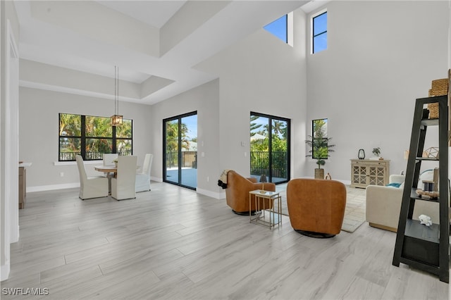 interior space featuring a towering ceiling, light wood finished floors, baseboards, and a tray ceiling