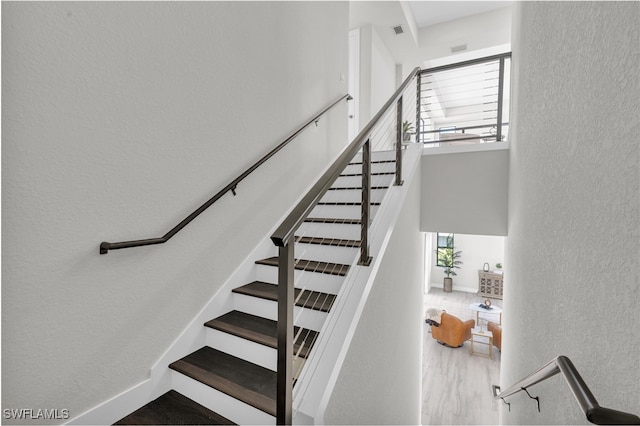 staircase featuring visible vents, a textured wall, a towering ceiling, wood finished floors, and baseboards