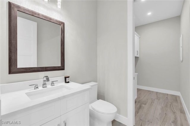 bathroom featuring toilet, baseboards, wood finished floors, and vanity