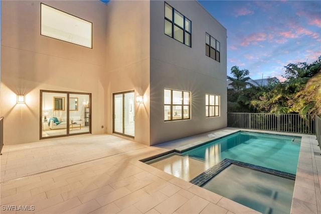 pool at dusk featuring a pool with connected hot tub, a patio area, and fence