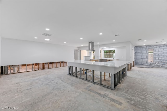 kitchen with island exhaust hood, a breakfast bar, brick wall, and a kitchen island