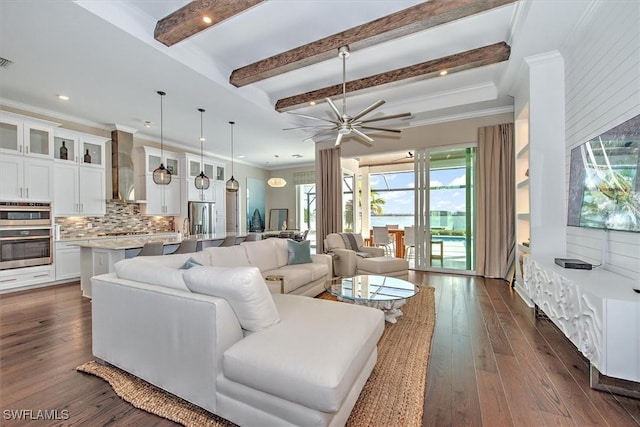 living area featuring dark wood finished floors, beam ceiling, ceiling fan, and ornamental molding