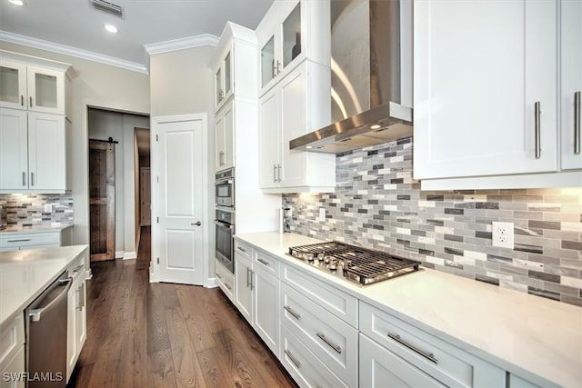 kitchen featuring white cabinetry, a barn door, wall chimney range hood, ornamental molding, and stainless steel appliances