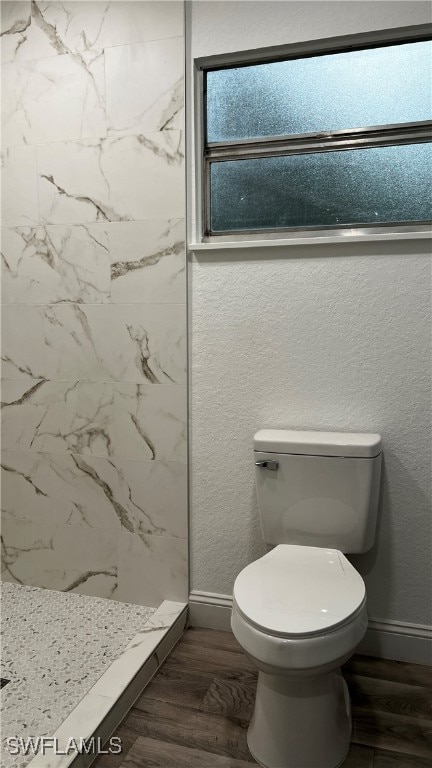 bathroom with a tile shower, hardwood / wood-style flooring, and toilet