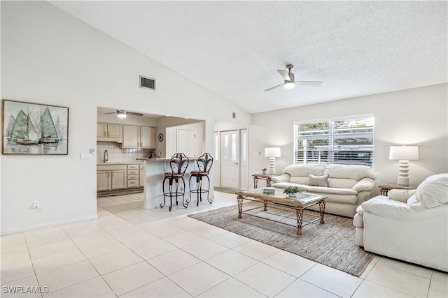 tiled living room featuring ceiling fan, high vaulted ceiling, a textured ceiling, and sink