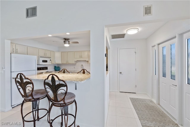 kitchen featuring backsplash, a breakfast bar, light stone countertops, light tile patterned flooring, and white appliances