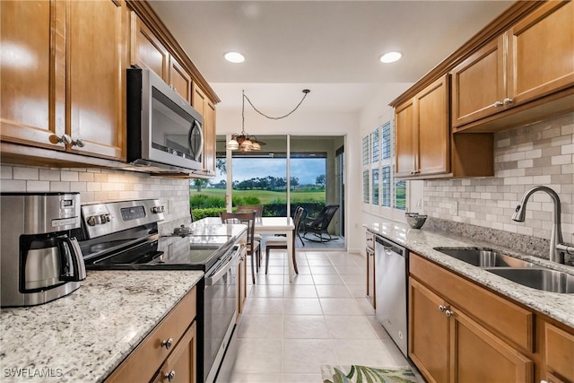 kitchen with sink, light tile patterned flooring, hanging light fixtures, appliances with stainless steel finishes, and light stone counters