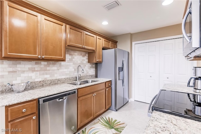 kitchen featuring stainless steel appliances, tasteful backsplash, light tile patterned flooring, light stone countertops, and sink