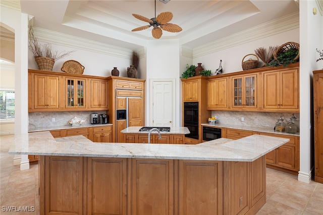 kitchen featuring tasteful backsplash, light stone counters, double oven, and a large island with sink