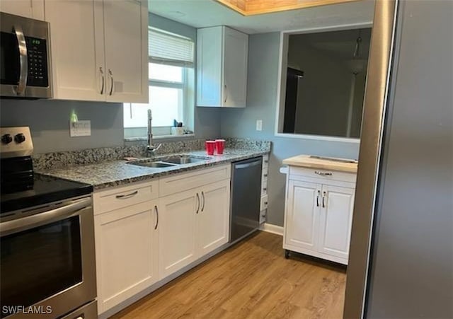 kitchen featuring stainless steel appliances, sink, white cabinets, light stone counters, and light hardwood / wood-style floors