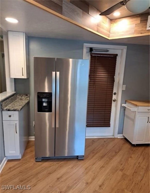 kitchen with white cabinetry, dark stone counters, light wood-type flooring, and stainless steel fridge