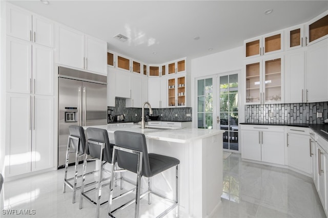 kitchen with stainless steel built in fridge, backsplash, an island with sink, and a kitchen breakfast bar