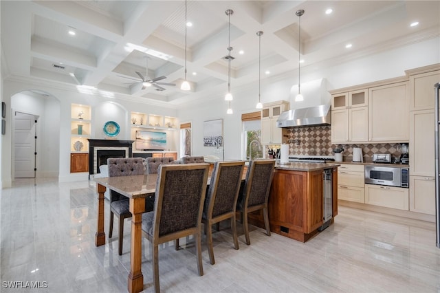 kitchen featuring ceiling fan, stainless steel microwave, a kitchen island with sink, a kitchen bar, and wall chimney exhaust hood