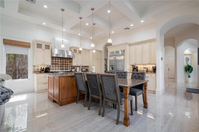 kitchen with an island with sink, hanging light fixtures, coffered ceiling, built in refrigerator, and beam ceiling