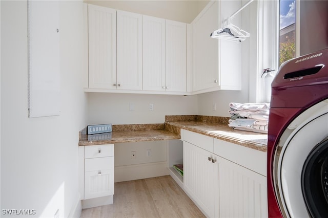 clothes washing area featuring washer / dryer, light hardwood / wood-style flooring, and cabinets