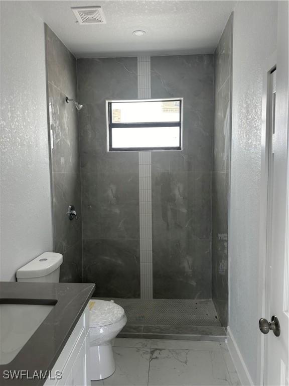 bathroom featuring tiled shower, vanity, and toilet