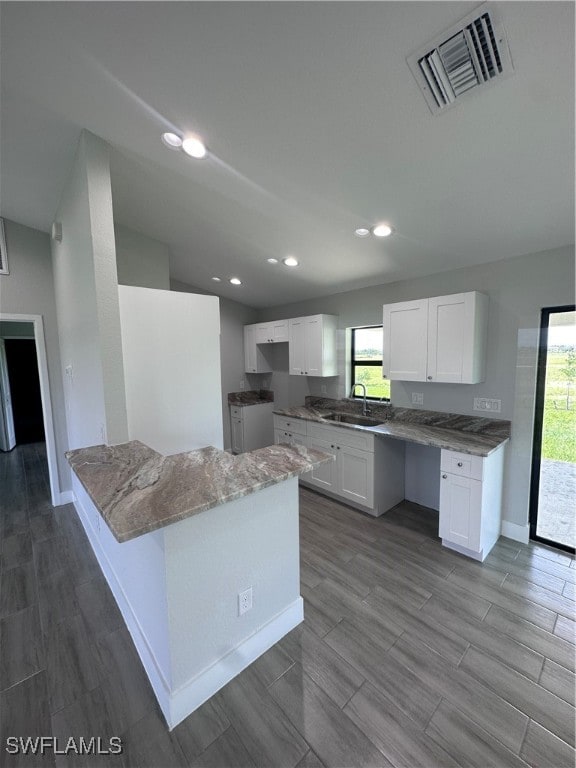 kitchen with light stone countertops, sink, a center island, white cabinetry, and light hardwood / wood-style flooring