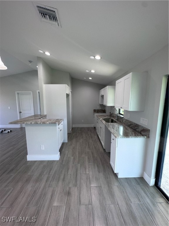 kitchen featuring lofted ceiling, dark stone countertops, sink, light wood-type flooring, and white cabinets