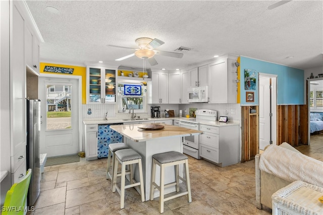 kitchen with plenty of natural light, white cabinetry, a kitchen bar, and white appliances