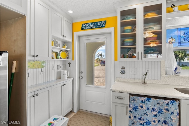 interior space featuring decorative backsplash, white cabinets, light stone counters, and a textured ceiling