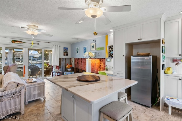 kitchen with white cabinets, stainless steel refrigerator, a kitchen island, and light stone counters