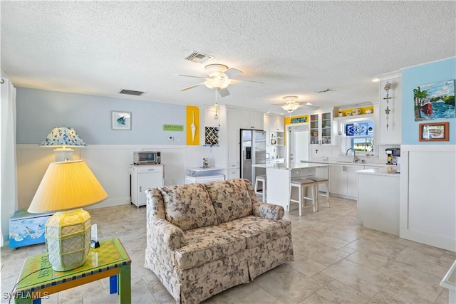 living room featuring ceiling fan, a textured ceiling, and visible vents