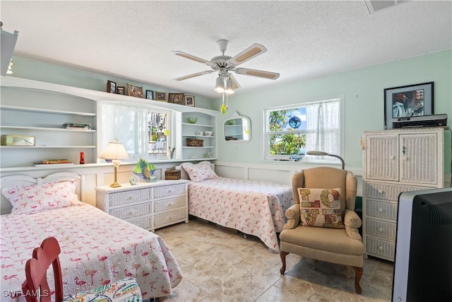 bedroom featuring a ceiling fan, visible vents, a decorative wall, and a textured ceiling