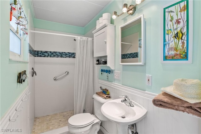 full bathroom with a stall shower, a wainscoted wall, a sink, and toilet