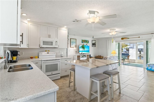 kitchen featuring a breakfast bar, white cabinetry, a kitchen island, a sink, and white appliances