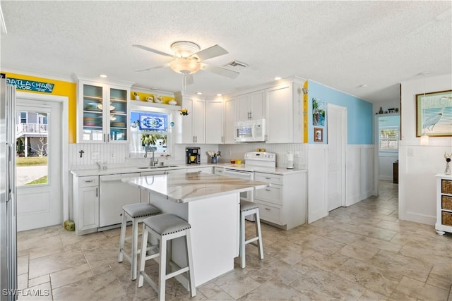 kitchen with white appliances, visible vents, white cabinets, a breakfast bar area, and a sink